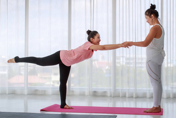 Tapasztalt női jógaoktató segédkezik a matracon álló kezdőknek, és gyakorolja a harcos pózt a megfelelő egyensúllyal a fitness stúdióban. Egészséges életmód és fitness koncepció - Fotó, kép