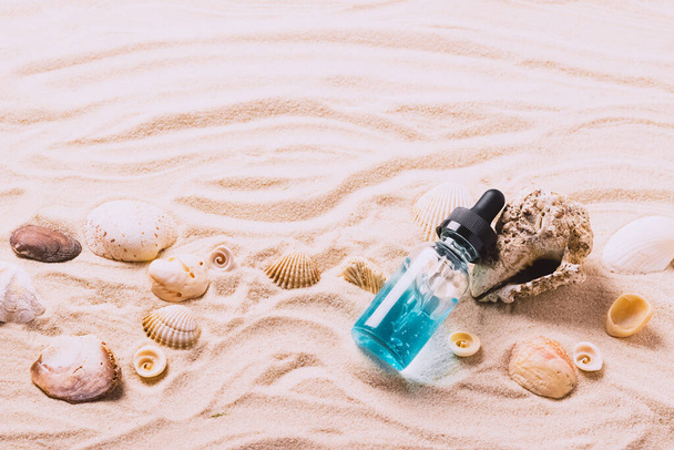 Glass bottle with serum gel cosmetic product air bubbles on the background seashells beach sand. Top view copy space. - Foto, imagen
