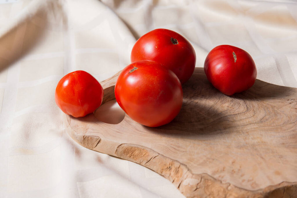 Четыре помидора лежат на разделочной доске из натурального оливкового дерева.  - Фото, изображение