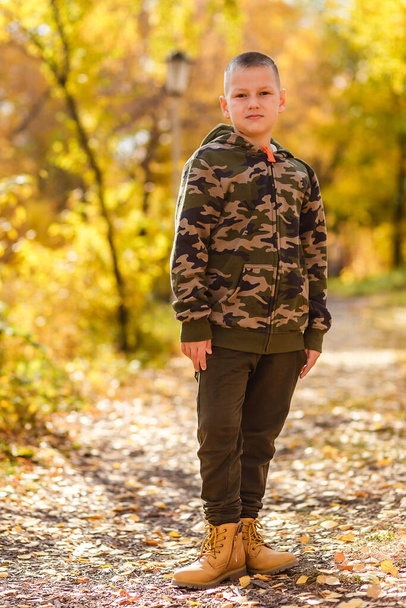 a nine-year-old boy in a camouflage suit stands in an autumn park - Photo, image