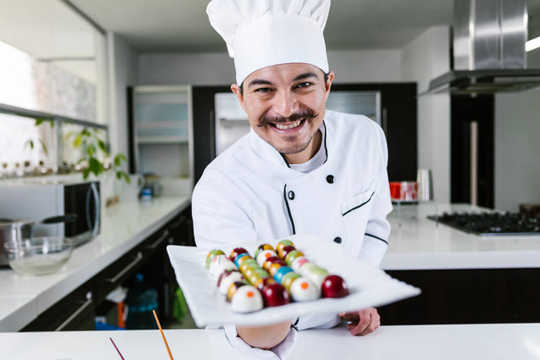 young latin man chocolatier in chef hat standing with mexican chocolates candies on plate in a commercial kitchen in Mexico Latin America - Photo, Image