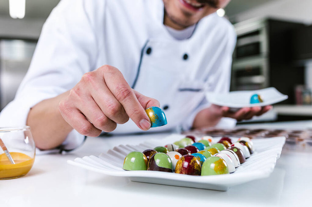 jovem latino chocolatier homem em chapéu de chef de pé com chocolates mexicanos doces na placa em uma cozinha comercial no México América Latina - Foto, Imagem