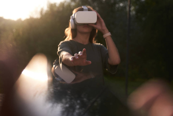 A girl holding virtual reality glasses on her head with her hands. He stretches out one hand to the camera, next to a beam of sunlight. - Photo, Image