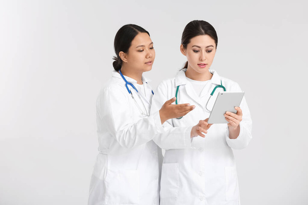 Portret van vrouwelijke Aziatische artsen met tablet op lichte achtergrond - Foto, afbeelding