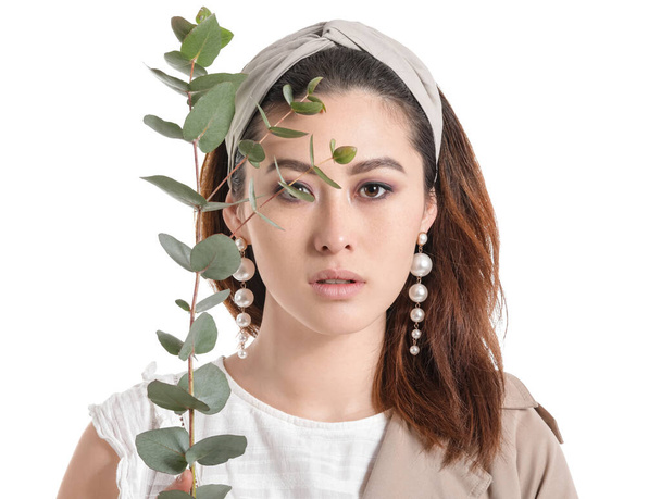 Beautiful young Asian woman with eucalyptus branch on white background - Photo, image