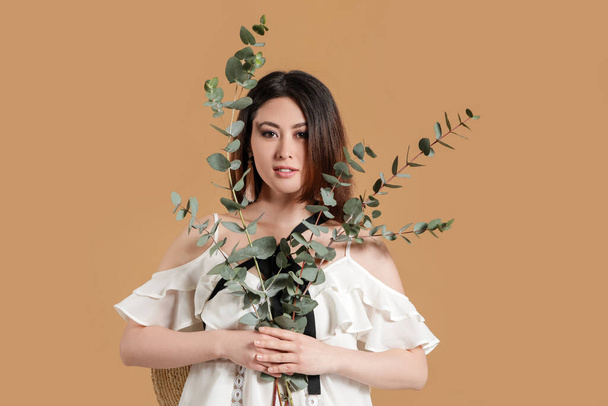 Beautiful young Asian woman with eucalyptus branches on color background - Photo, Image