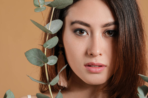 Beautiful young Asian woman with eucalyptus branch on color background - Photo, image