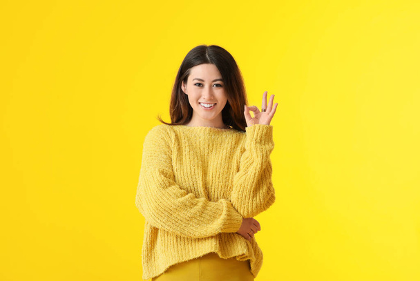Schöne junge asiatische Frau zeigt OK auf gelbem Hintergrund - Foto, Bild