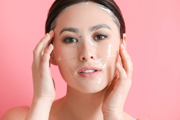 Hermosa joven mujer asiática con máscara facial de hoja en el fondo de color - Foto, Imagen