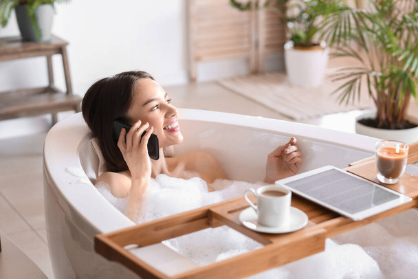 Evde banyo yaparken cep telefonuyla konuşan genç bir kadın. - Fotoğraf, Görsel
