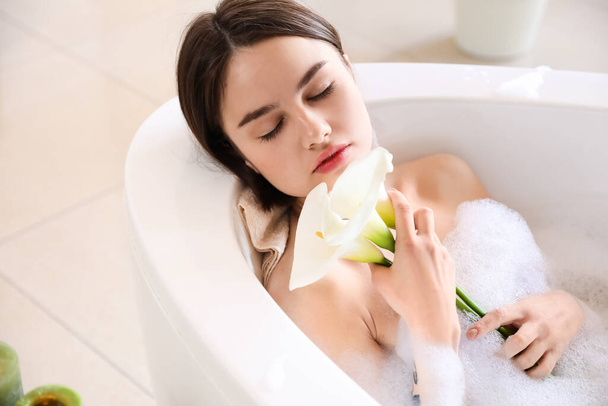 Молода жінка з красивими кальянними ліліями приймає розслаблюючу ванну вдома
 - Фото, зображення