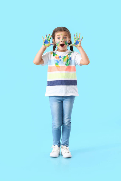 Verrast klein meisje in verf op blauwe achtergrond - Foto, afbeelding
