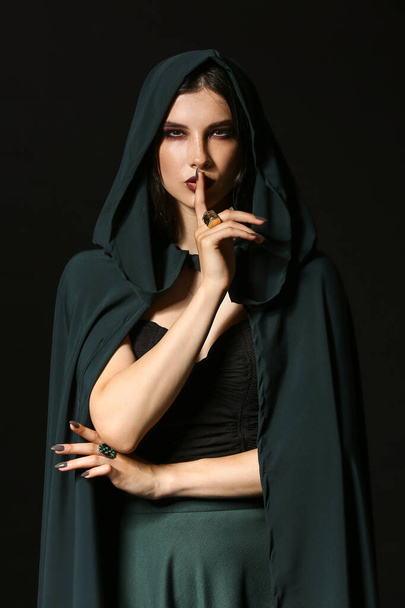 Junge Hexe zeigt Schweigegeste auf dunklem Hintergrund - Foto, Bild