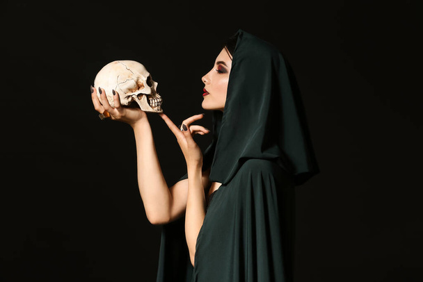 Bruxa jovem com crânio humano no fundo escuro - Foto, Imagem