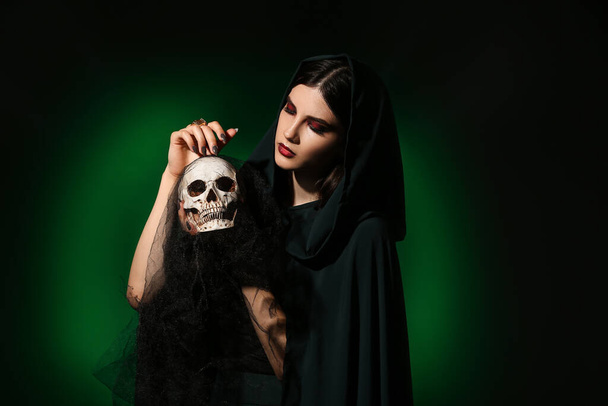 Young witch with skull on dark color background - Photo, Image