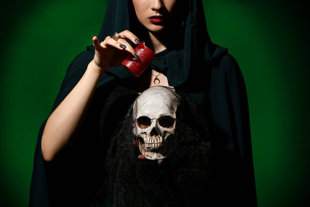 Jeune sorcière avec crâne et bougie sur fond de couleur sombre - Photo, image