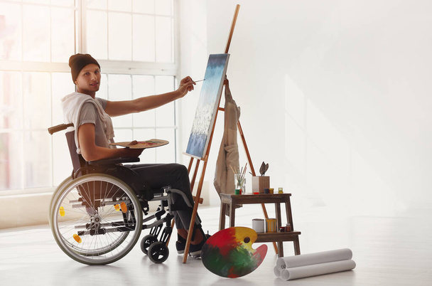Молодой художник-инвалид живописи в мастерской - Фото, изображение