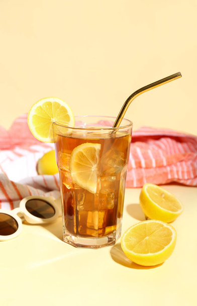 Glass of refreshing Long Island iced tea with lemon, sunglasses and towel on color background - Photo, Image
