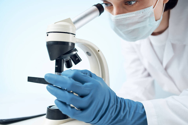 assistente di laboratorio indossando una maschera medica guardando attraverso un microscopio esperimento di ricerca professionale - Foto, immagini