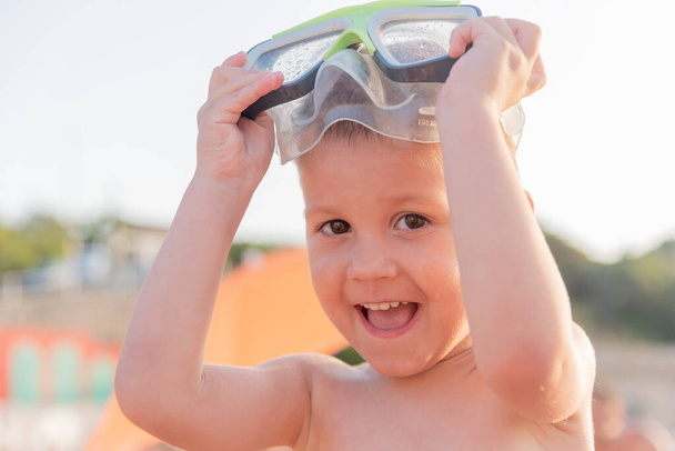 Крупный план счастливого смеющегося мальчика в водолазной маске на солнечном пляже. Мальчик в море в водолазной маске - Фото, изображение