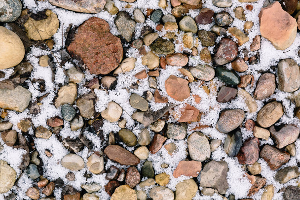 First snow or hail covered stones. Textured background. The track pattern made of natural material. Red and gray colors pebbles on a beach in winter season. Covering the pedestrian area. Garden path. - 写真・画像