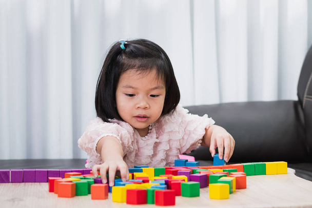 テーブルの上で木のブロックを演奏する小さな子供の女の子。おもちゃのブロックで幸せな子供の建物の建設。遊びを通じた学びと発展. - 写真・画像