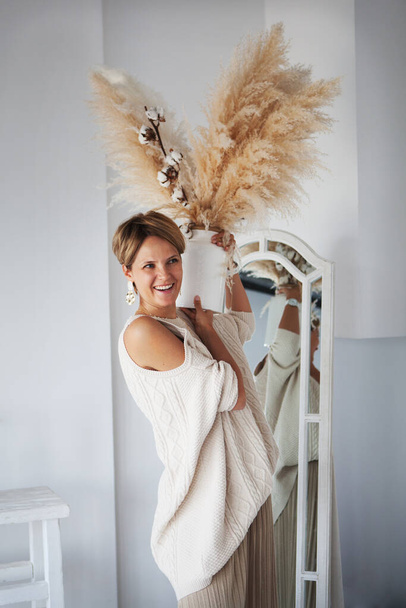 Beautiful interior designer decorates the new house with a bouquet of cotton and dry grass. Woman happy and laughing, having fun feeling, enjoy positive emotions - 写真・画像