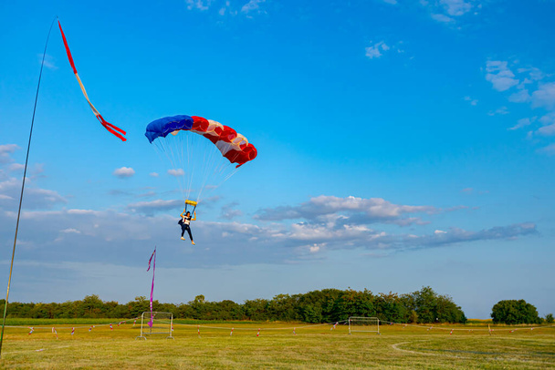 Parachutiste avec un parachute ouvert vole et ralentit pour atterrir au sol. parachutisme, vol plané, saut en parachute. Indicateur de ruban rouge et blanc indique la direction du vent - Photo, image