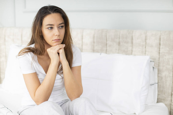 Lonely young woman sitting on bed. Depressed woman at home, looking away with sad expression - Foto, Bild
