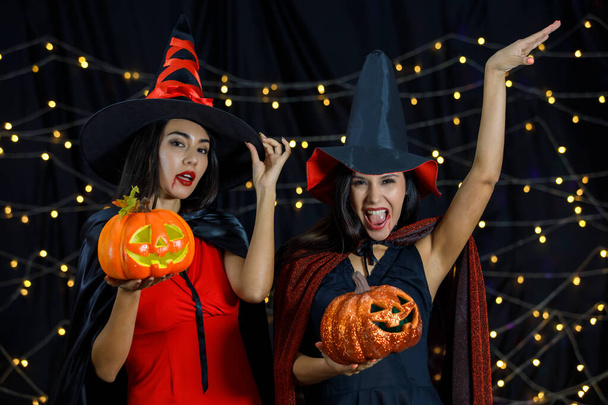 Fiatal női barátok boszorkány ruhák és kalapok tök fej a kezében szórakozás Halloween ünnepe az éjszakai party - Fotó, kép
