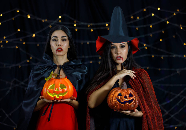 Tunnistamattomia tyttöystäviä noitapuvuissa, jotka peittävät kasvot kurpitsapäillä yön aikana Halloween-juhlissa - Valokuva, kuva