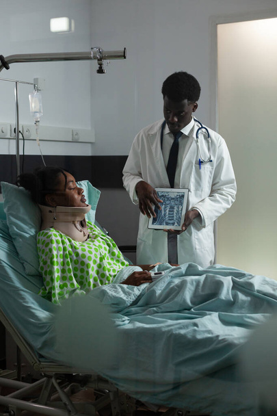 Médico de etnia africana que muestra resultados de rayos X a paciente joven - Foto, imagen