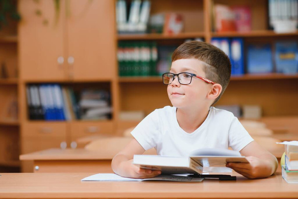 Elementary school boy at classroom desk trying to find new ideas for schoolwork. - Foto, Bild