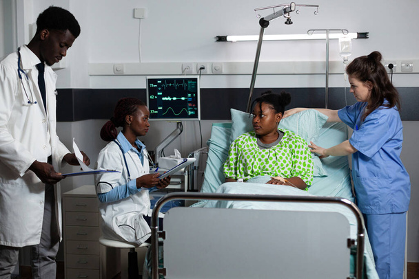 Multi-etnische medische team consulting jonge persoon in het ziekenhuis afdeling - Foto, afbeelding