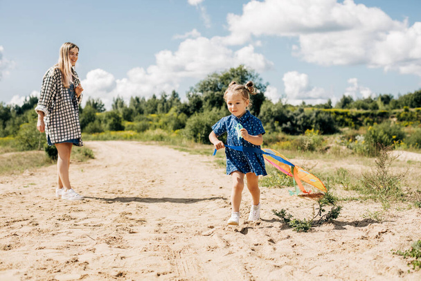 A little girl flies a kite with her older sister and runs away from her - Foto, Bild
