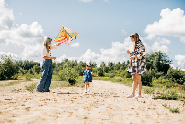 Мать запускает воздушного змея со своими дочерьми во время семейного отдыха в стране - Фото, изображение