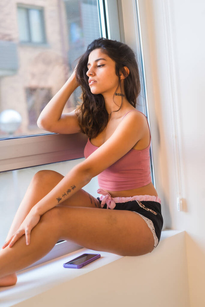 Stile di vita, rilassato bruna ragazza caucasica in pigiama accanto a una finestra in posa guardando la fotocamera - Foto, immagini