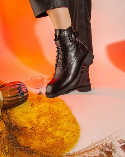 Γυναικείες φθινοπωρινές μαύρες δερμάτινες μπότες με πόδια σε έγχρωμο φόντο στούντιο πυροβόλησε. - Φωτογραφία, εικόνα