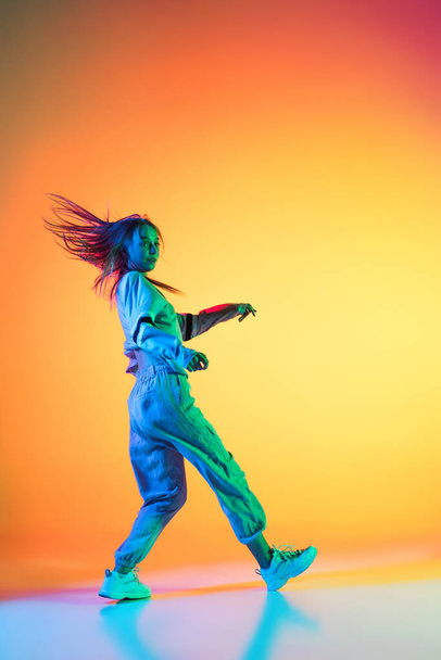 Young sportive girl dancing hip-hop in stylish clothes on colorful background at dance hall in neon light. Youth culture, movement, style and fashion, action. - Foto, immagini