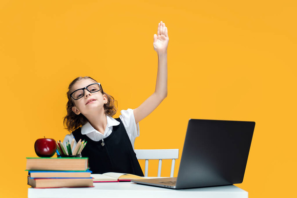 Beyaz liseli kız elini kaldırdı. Öğrenci çevrimiçi ders sırasında dizüstü bilgisayarın başına oturur. Uzak Okul Öğrenimi. - Fotoğraf, Görsel