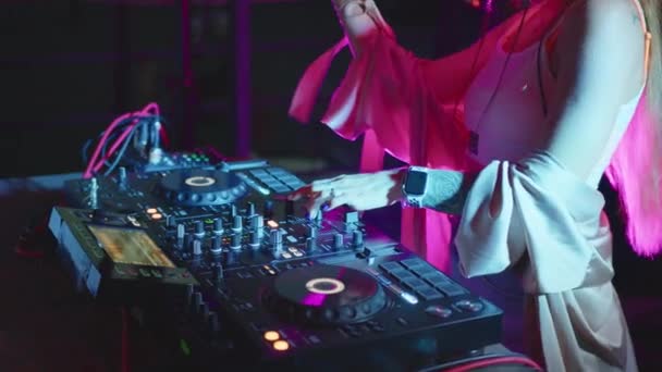 DJ kezek irányítják a hangkonzolt a zene keveréséhez a diszkóklubban. Lassított felvétel. Az ujjak megérintik a gombokat, elektronikus zenét játszanak a fedélzeten. Színes fények mutatják a nightclub tánc party. - Felvétel, videó