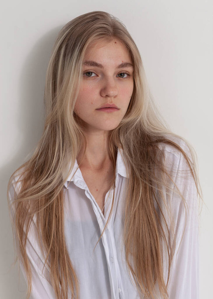 portrait of a beautiful blonde with long hair in a white shirt on a light background - Zdjęcie, obraz