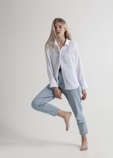 beautiful blonde in a white shirt and jeans on a gray background - Zdjęcie, obraz