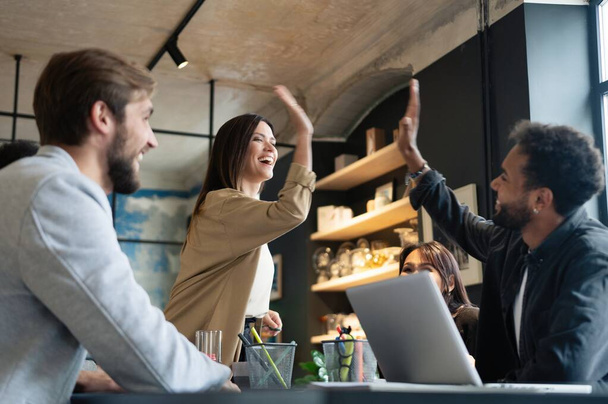 Two cheerful young business people giving high-five while their colleagues looking at them and smiling. - Foto, afbeelding