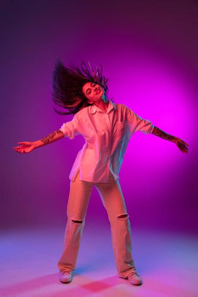 Portrait of Latino beautiful happy girl dancing isolated on purple, lilac color studio background in neon light. Concept of human emotions, facial expression - Foto, immagini