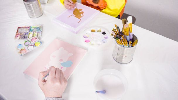 Kleines Mädchen malt mit Acrylfarbe auf Leinwand mit ihrer Mutter für ein Kunstprojekt im Fernunterricht. - Foto, Bild