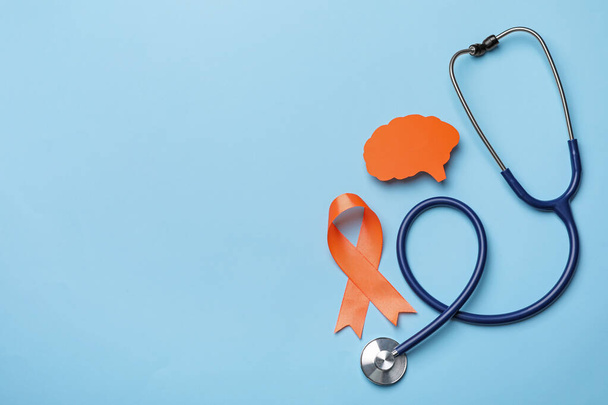 Orange ribbon, stethoscope and paper brain cutout on light blue background, flat lay with space for text. Multiple sclerosis awareness - Fotó, kép