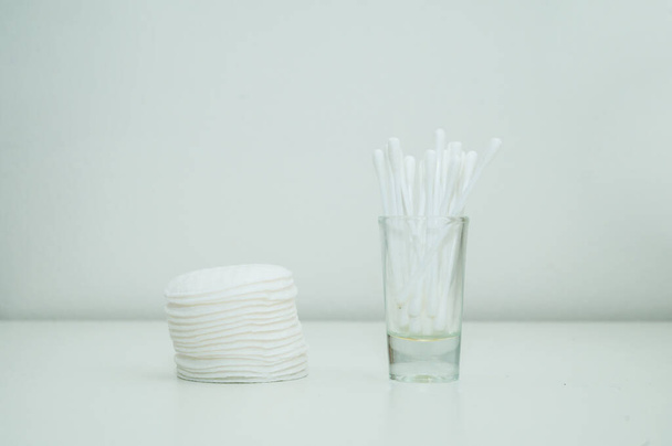 Close-up of stack of cotton pads and cotton swabs in a glass cup. White background. - Foto, imagen