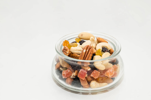 Орехи, засахаренные фрукты, сушеные ягоды в стеклянной миске. Здоровая вегетарианская еда. Кешью, бразильские орехи, изюм. - Фото, изображение