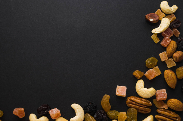 Pähkinät ja kuivatut marjat, jotka on asetettu mustalla pohjalla olevan kehyksen muodossa. cashewpähkinät, brasilianpähkinät, sokeroidut hedelmät. - Valokuva, kuva